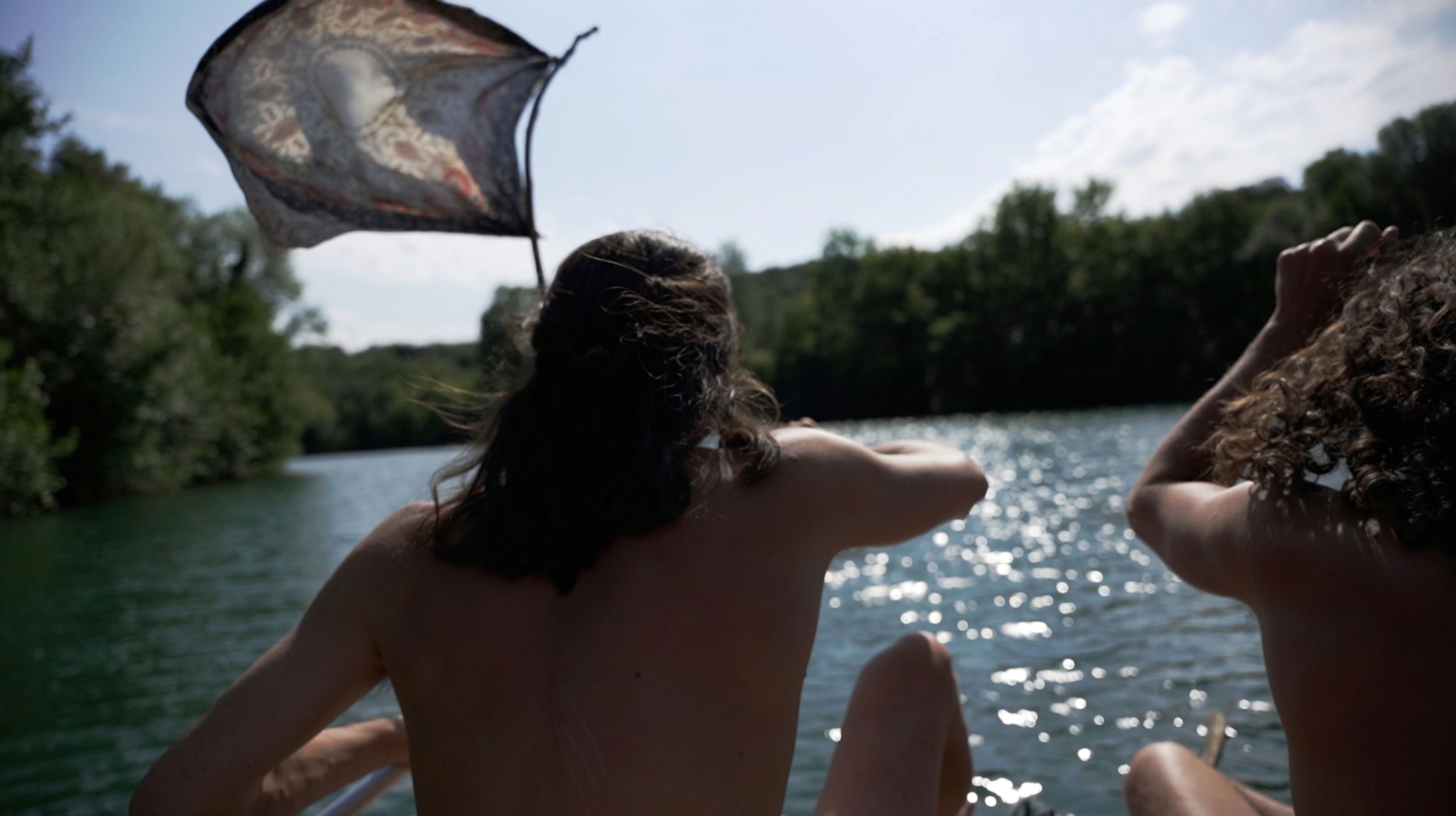 Photo de deux personnes de dos sur un bateau regardant l'eau et agitant un drapeau