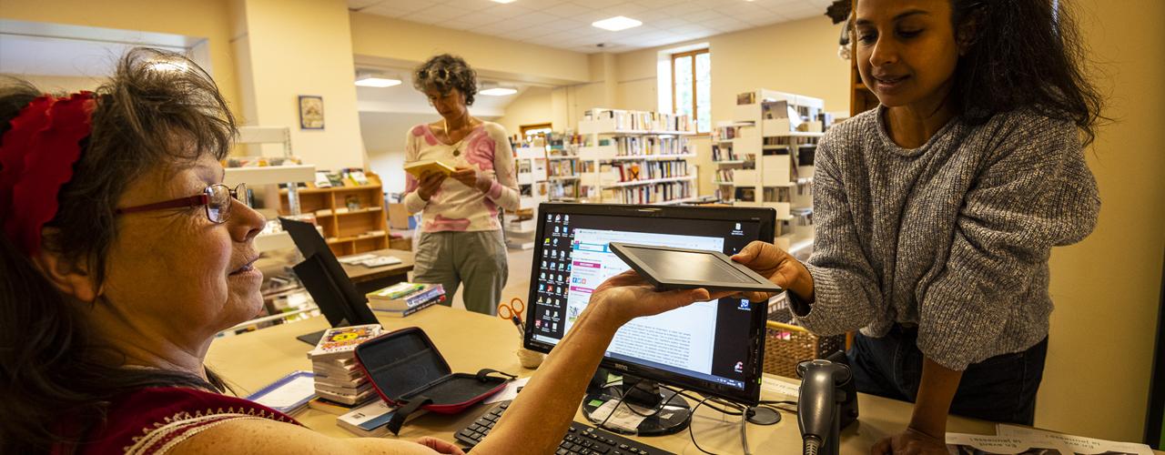 Une bibliothécaire tend une liseuse électronique à une jeune fille.