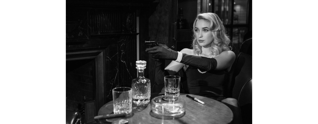 photo de femme en noir et blanc assise et visant avec un pistolet extrait d'un film