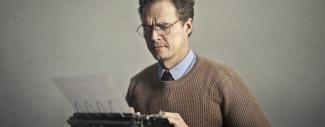 Écrivain mâle adulte sourcils froncés travaillant sur machine à écrire à la maison.