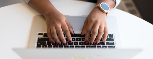 mains de femme vue du dessus tapant sur un clavier d'ordinateur